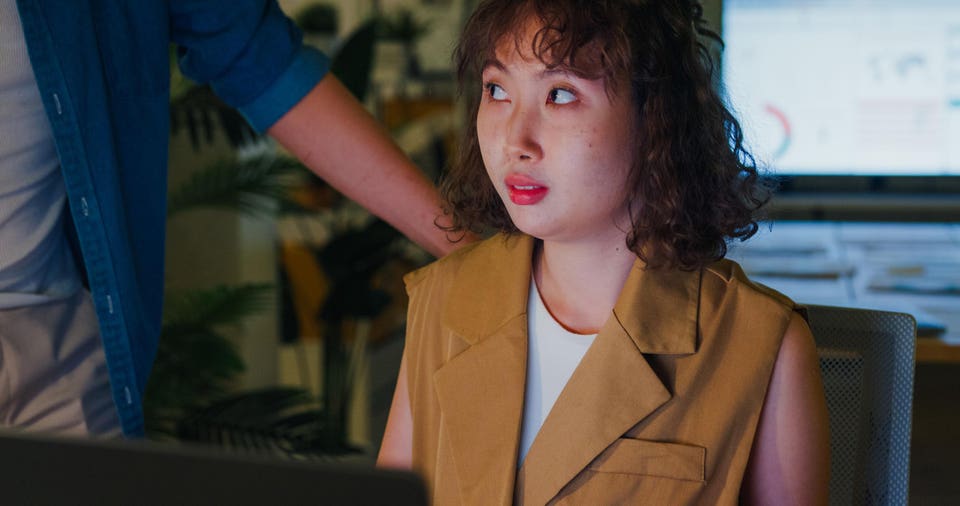 Asian male Manager accusingly expressing displeasure to young female employee suggesting a tense workplace situation in office at night. ESG sustainable business office.